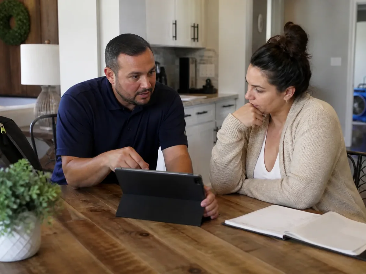 A TruePoint representative at a kitchen table walking a homeowner through her insurance claim paperwork on a tablet