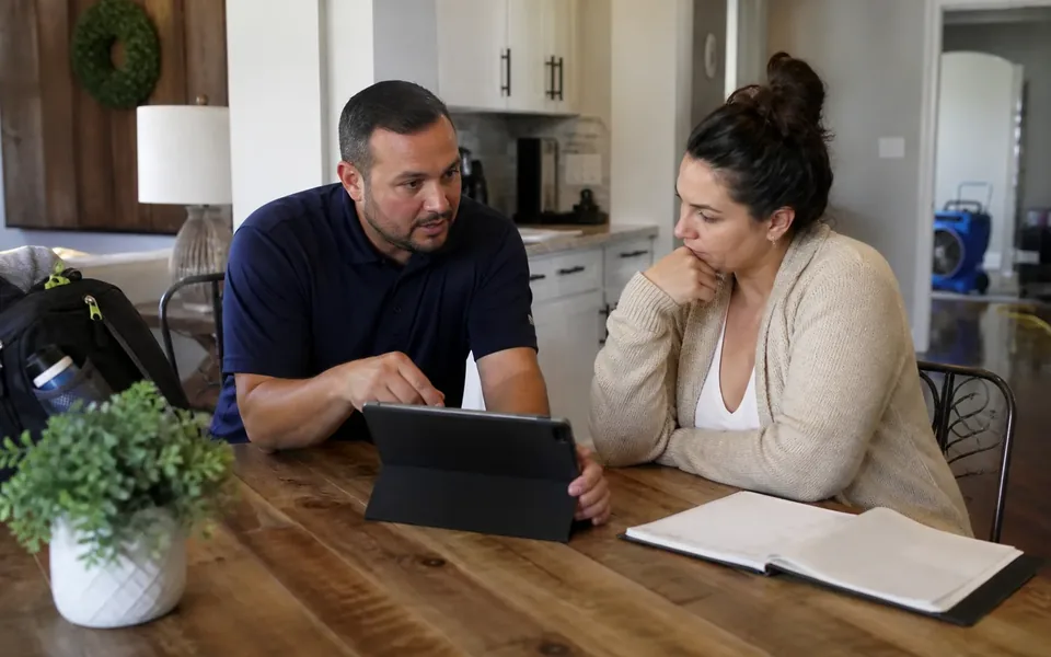 TruePoint representative at a kitchen table reviewing insurance claim paperwork with a homeowner